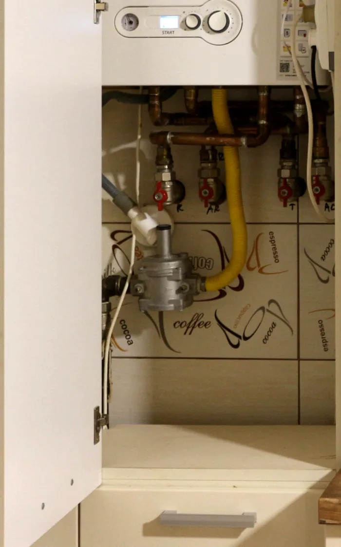 Wall-mounted residential gas boiler and connected piping inside a kitchen cabinet