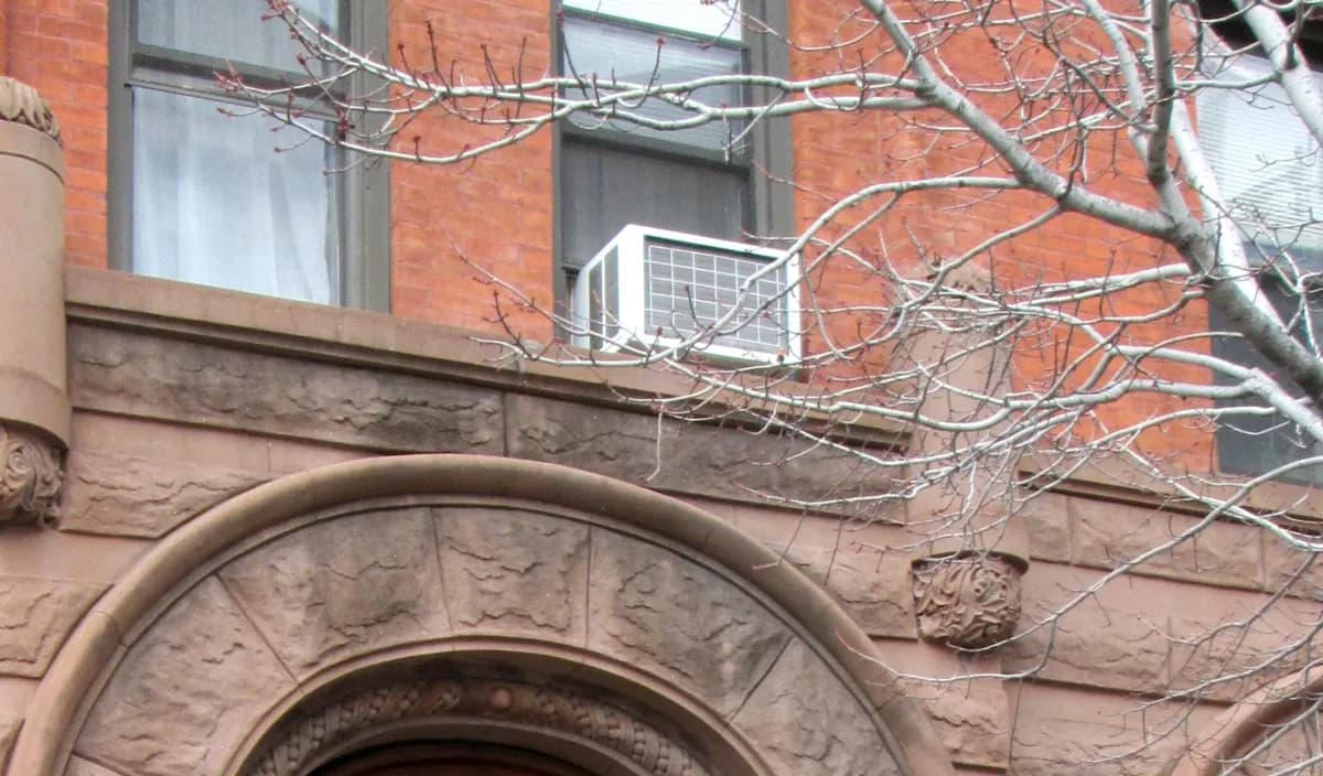 Window air conditioner in an upper-floor window of a brick and brownstone apartment building in Prospect Heights, Brooklyn