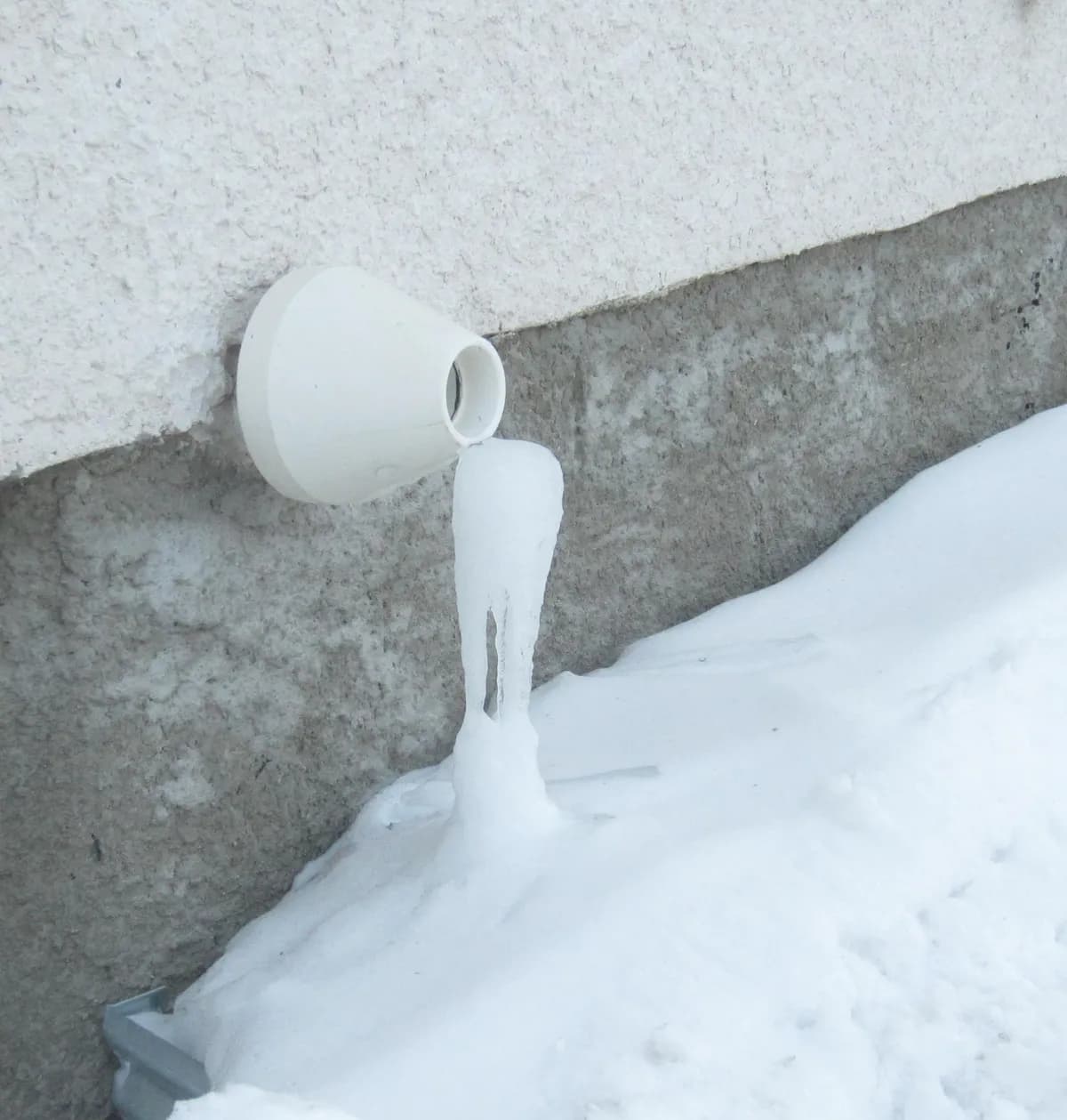 Plastic exhaust vent of a high-efficiency gas furnace on an outside wall, with ice built up below it