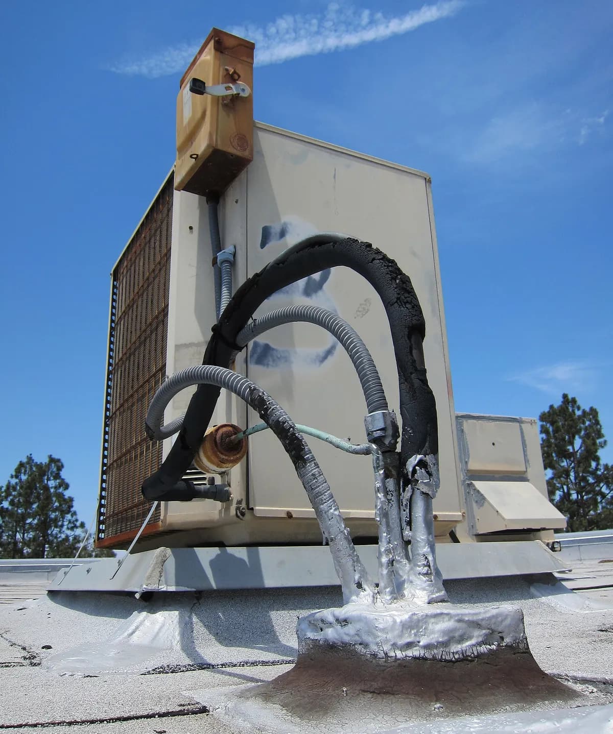 Air conditioning condensing unit on a flat roof, with insulated refrigerant lines, electrical conduit and a disconnect box